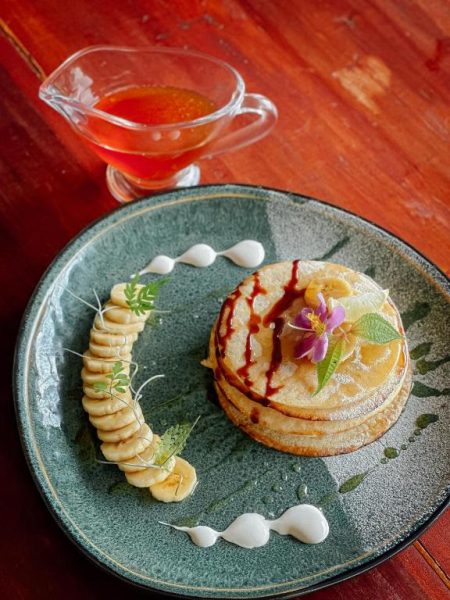 Pancakes con rodajas de plátano, flor comestible y salsa de frutos rojos en Eco Vibe Resort