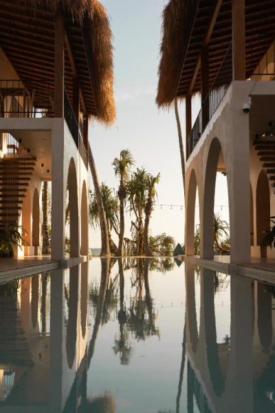Piscina infinity con arcos blancos y palmeras tropicales al atardecer en Neem Boutique Hotel Madiha