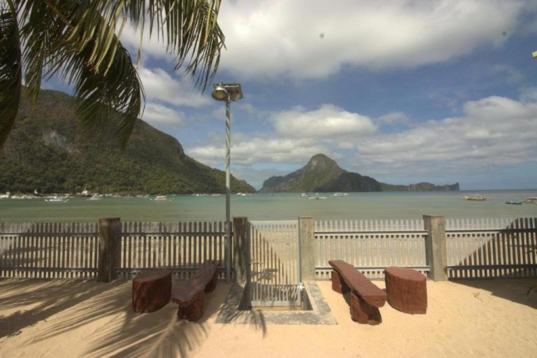Vista panorámica de la bahía con montañas desde la playa del Chislyk Inn con bancos de madera