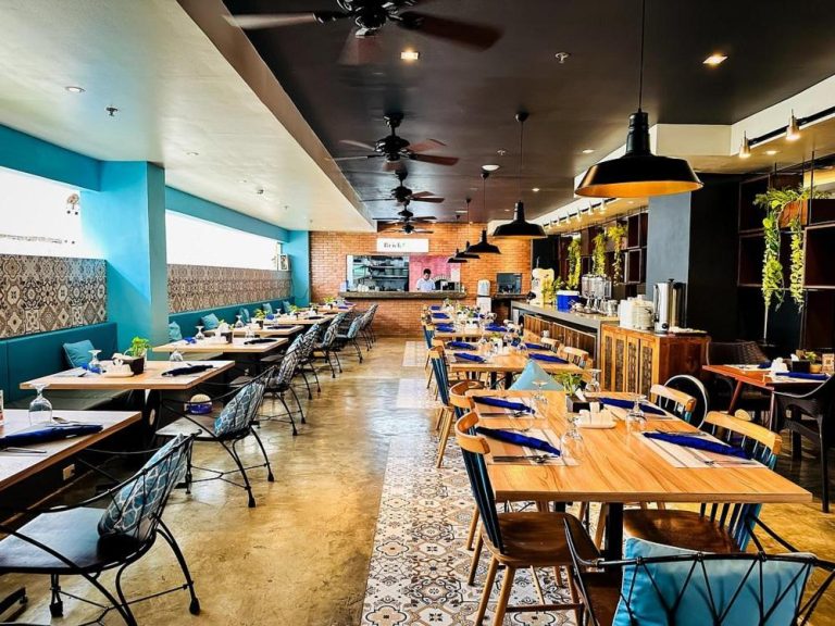 Restaurante interior del Ferra Hotel and Garden Suites con mesas de madera, decoración azul y cocina abierta