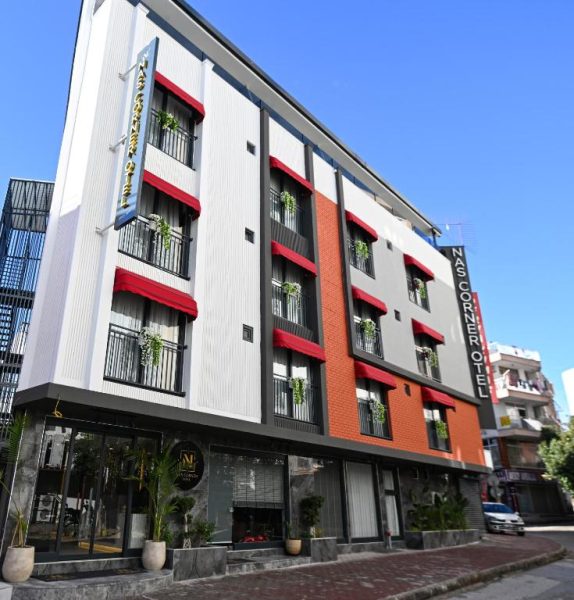 Fachada exterior del Nas Corner Hotel con toldos rojos y balcones con plantas decorativas
