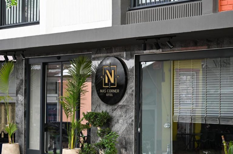 Fachada exterior y entrada principal del Nas Corner Hotel con logo dorado y plantas decorativas