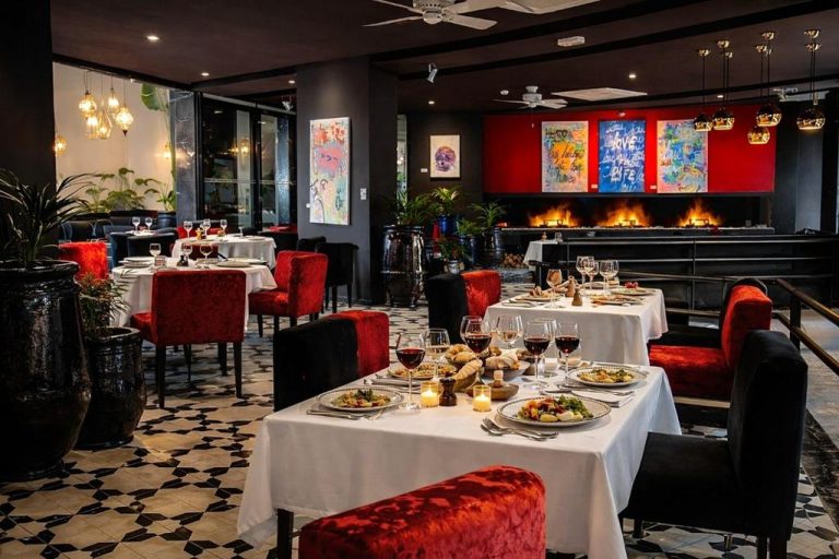 Elegante restaurante del Bab Hotel Marrakech con sillas rojas, mesas servidas y chimenea decorativa al fondo