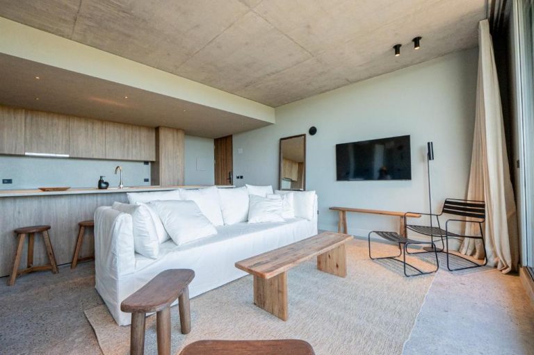 Salón moderno con sofá blanco y cocina abierta en CasaChica Hotel, decoración minimalista en tonos naturales