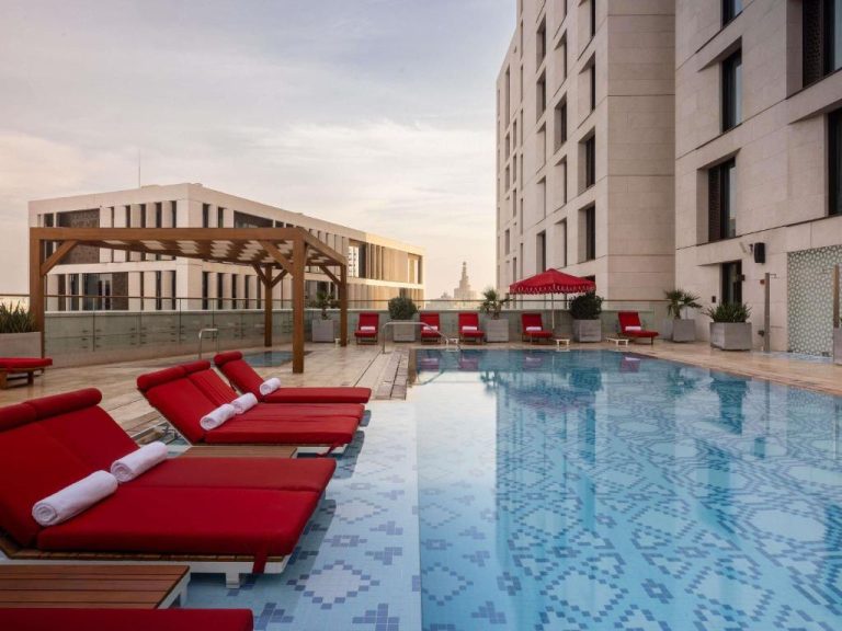 Piscina exterior con tumbonas rojas en la terraza del Alwadi Hotel Doha MGallery Collection en Qatar