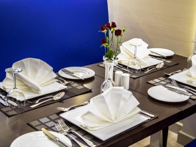 Mesa de restaurante elegantemente decorada con servilletas y rosas rojas en Gulf Pearls Hotel