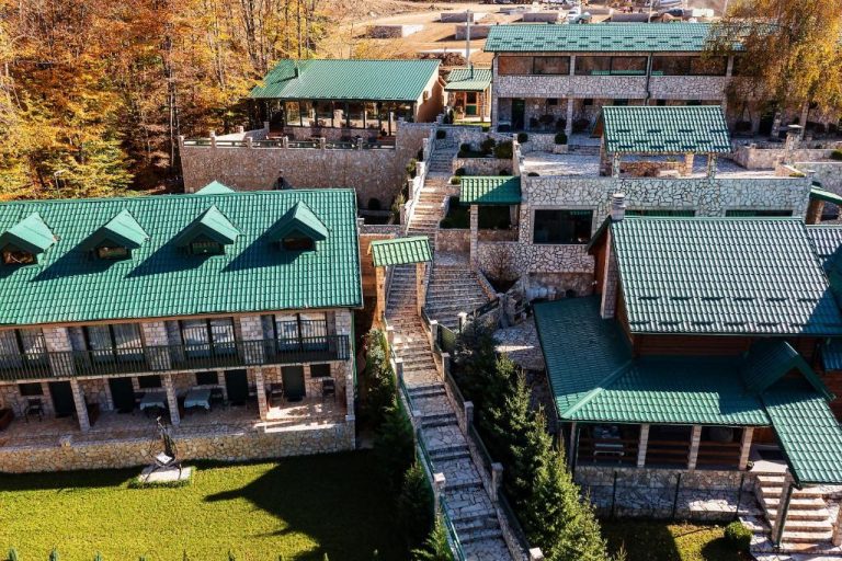 Vista aérea del Garni Hotel Elite Resort con tejados verdes y arquitectura de piedra entre bosque otoñal