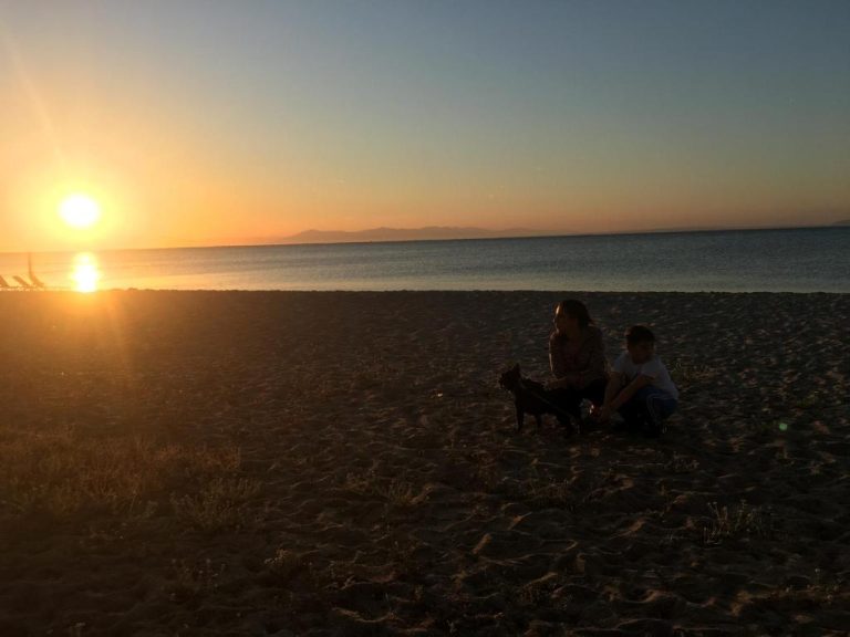 Pareja con perro disfrutando del atardecer en la playa del Hotel Anemos con vistas al mar