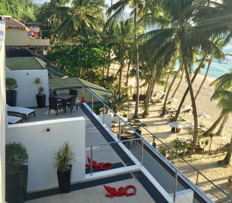 Terraza con tumbonas y vistas a la playa de arena blanca y palmeras en Sundown Beach Studios
