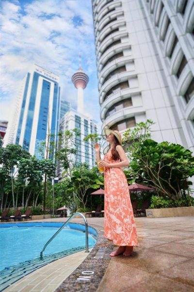 Mujer junto a la piscina exterior del Shangri-La Kuala Lumpur con vistas a la Torre KL al fondo
