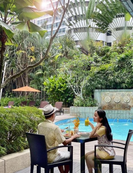 Pareja disfrutando de cócteles junto a la piscina tropical del Shangri-La Kuala Lumpur