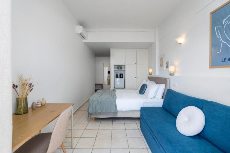 Estudio moderno con sofá azul y cama doble en el Hotel Flisvos, decoración minimalista en tonos blancos