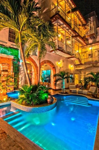 Piscina iluminada de noche con palmeras tropicales y arquitectura colonial del Hotel Boutique Don Pepe