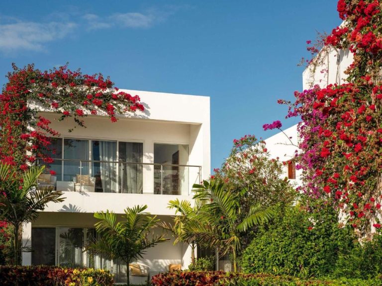 Fachada exterior blanca del Nungwi Dreams by Mantis rodeada de buganvillas rojas y jardines tropicales