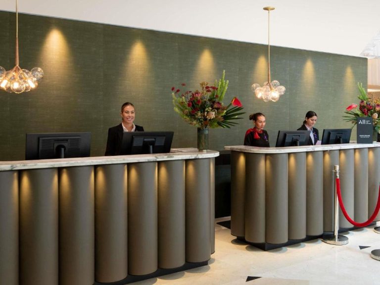 Recepción moderna del Swissotel Sydney con tres recepcionistas y mostrador de mármol iluminado
