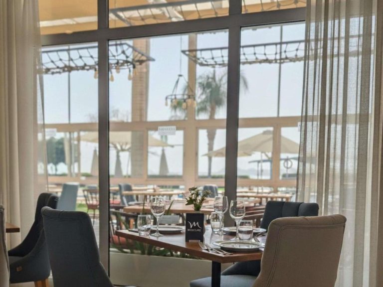 Restaurante interior con mesas elegantes y vistas al jardín y playa del Mercure Ismailia Forsan Island