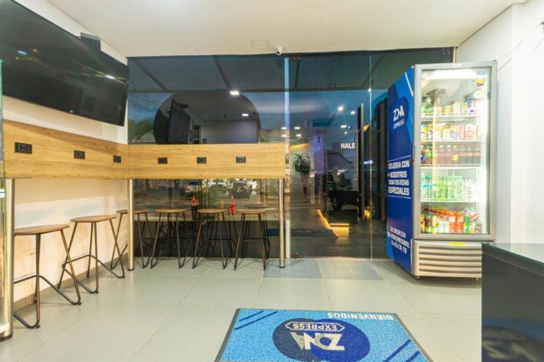 Área de bar y recepción con nevera de bebidas y pantallas en Hotel Zona Express San Diego