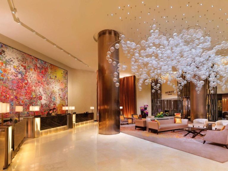 Lujoso lobby del Fairmont Singapore con araña de cristal y gran mural artístico colorido