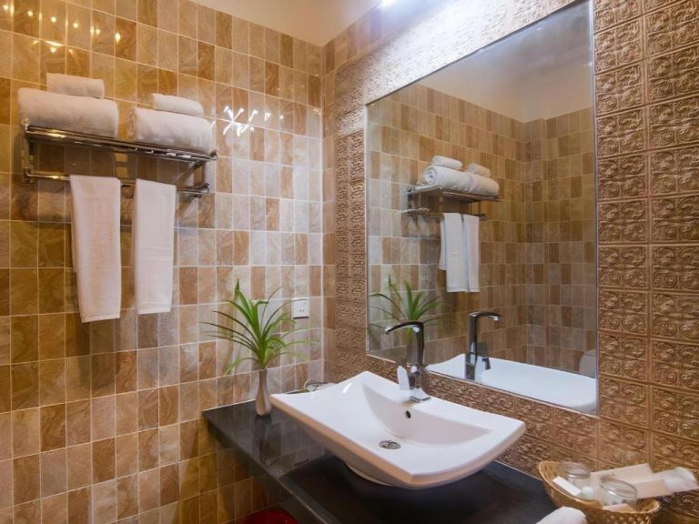 Baño elegante con lavabo moderno, espejo grande y azulejos dorados en Sambopich Chenla Hotel