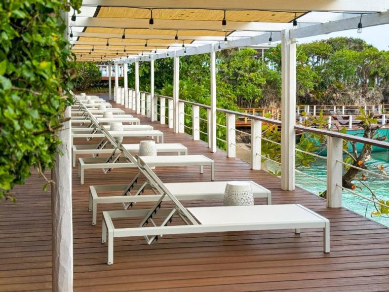 Terraza solarium con tumbonas blancas frente a la piscina en Hotel Roatán Media Luna Resort Meliá