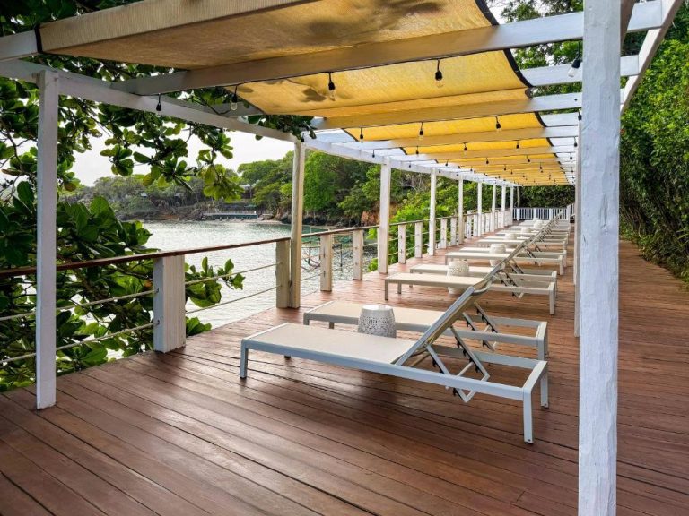 Terraza con tumbonas blancas sobre el mar en Hotel Roatán Media Luna Resort affiliated by Meliá