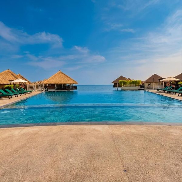 Piscina infinita con bungalows de techo de paja y vistas al mar en Golden Palm Tree Suite Sepang