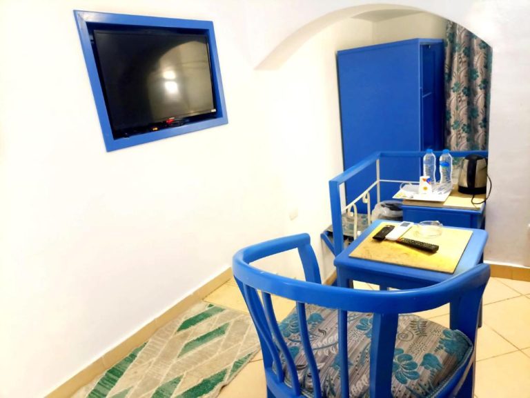 Habitación del Kanabesh Hotel con sillas y mesa azul, televisión en pared y armario azul