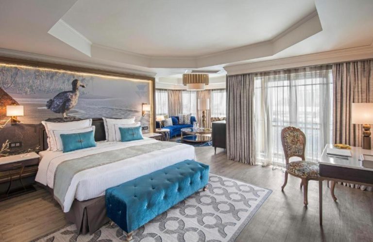 Suite de lujo con cama king, banco turquesa y mural del dodo en Labourdonnais Waterfront Hotel