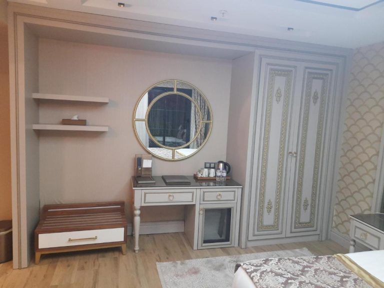 Habitación elegante con escritorio, espejo redondo dorado y armario clásico en Elysium Green Suites