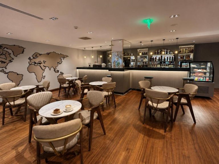 Cafetería y bar del The Revia Square Hotel con mesas de mármol, sillas modernas y decoración de mapa mundial