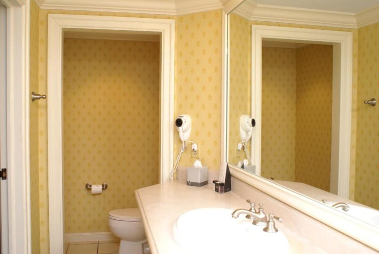Baño clásico del Columbia Club con lavabo, espejo amplio y papel pintado amarillo elegante
