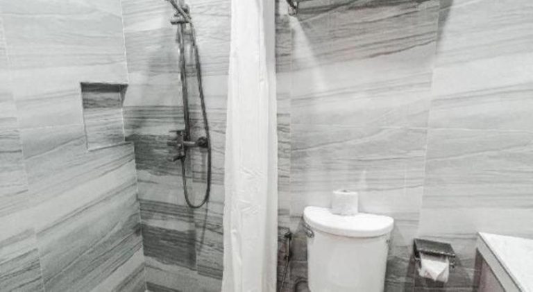Baño completo con ducha y cortina blanca en Lavero Suites, revestido con elegantes azulejos grises
