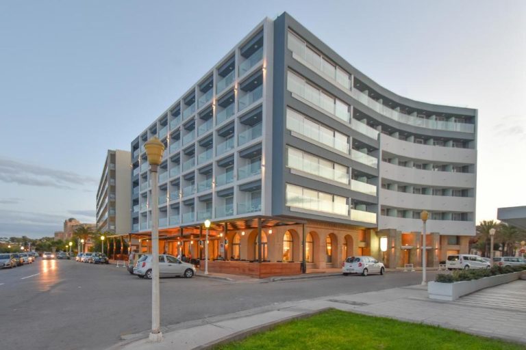 Fachada exterior del Ibiscus Hotel con arquitectura moderna y arcos en la planta baja al atardecer