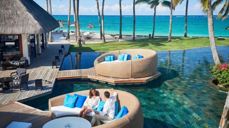 Pareja relajándose junto a la piscina infinita con vistas al mar turquesa del Constance Belle Mare Plage