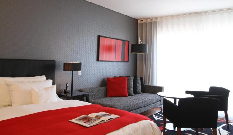 Habitación superior con cama king y sofá en el Fierro Hotel Buenos Aires, decoración en rojo y gris