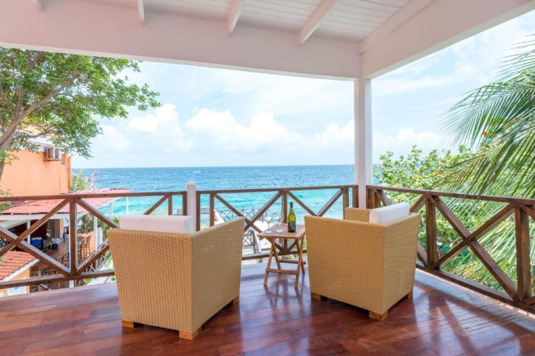 Terraza con sillones de ratán y vistas al mar turquesa en Scuba Lodge City Beach