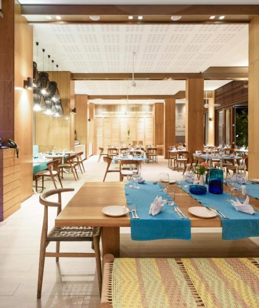 Restaurante interior del Eden Bleu Hotel con mesas de madera y mantelería azul turquesa en ambiente tropical