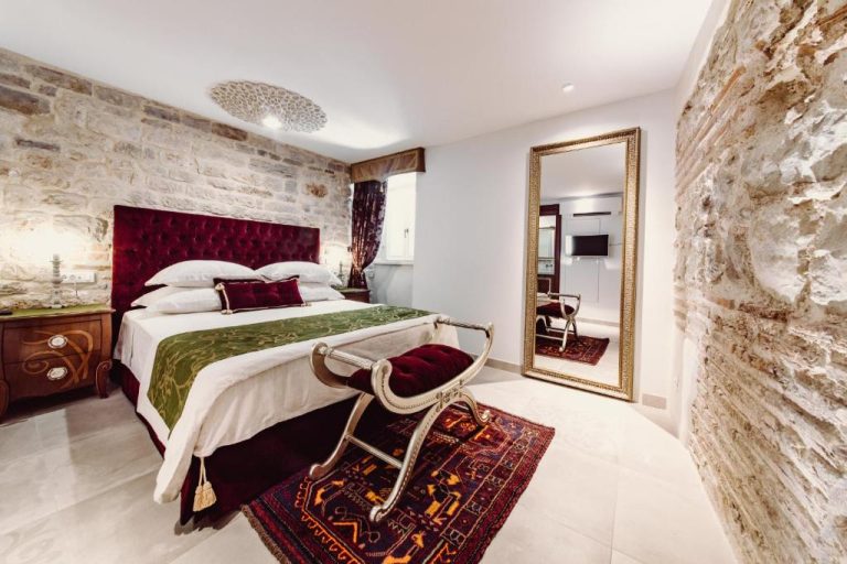 Habitación de lujo con cabecero rojo y pared de piedra natural en Villa Nepos Hotel