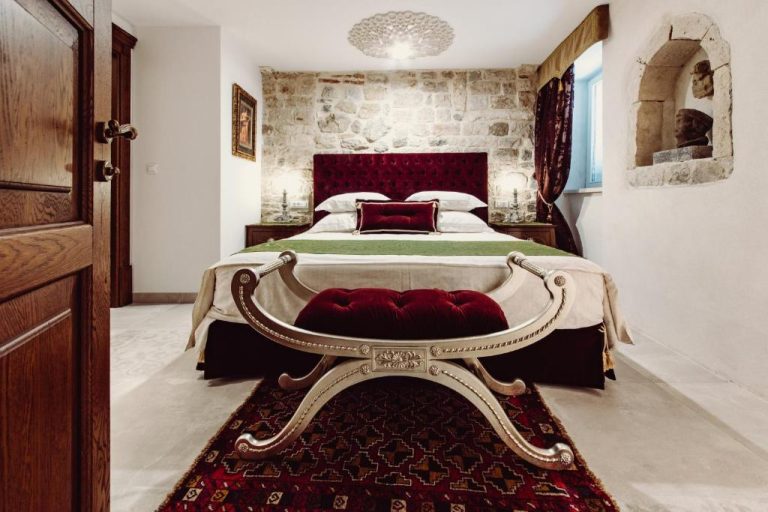 Habitación doble de lujo con cama tapizada en terciopelo rojo y pared de piedra en Villa Nepos Hotel