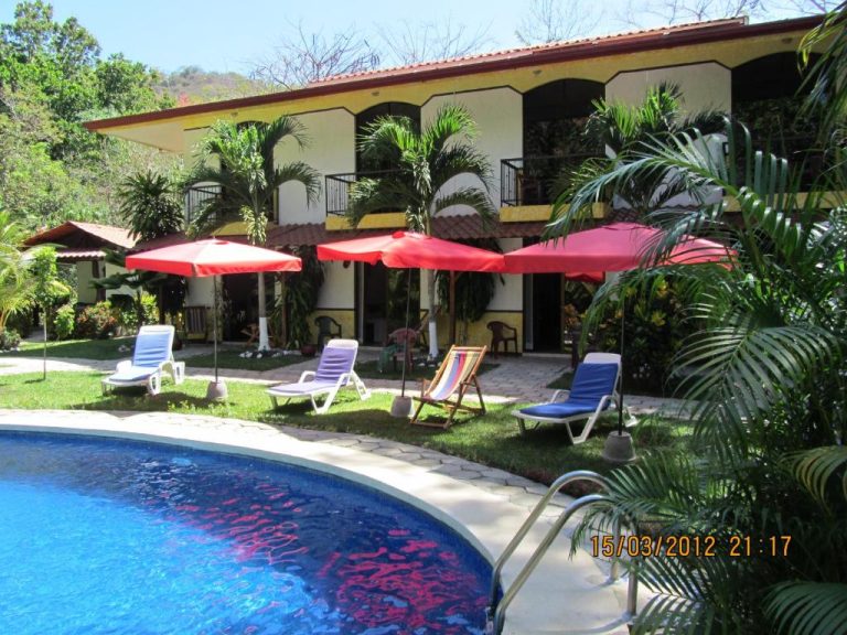 Piscina exterior con tumbonas y sombrillas rojas del Hotel Belvedere en Playa Samara, Costa Rica