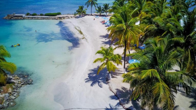 Vista aérea de la playa de arena blanca con palmeras y aguas turquesas del Canella Beach Hotel