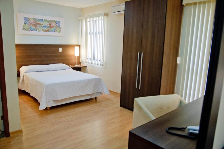Habitación doble con cama matrimonial y armario de madera en Mont Blanc Apart Hotel Nova Iguaçu