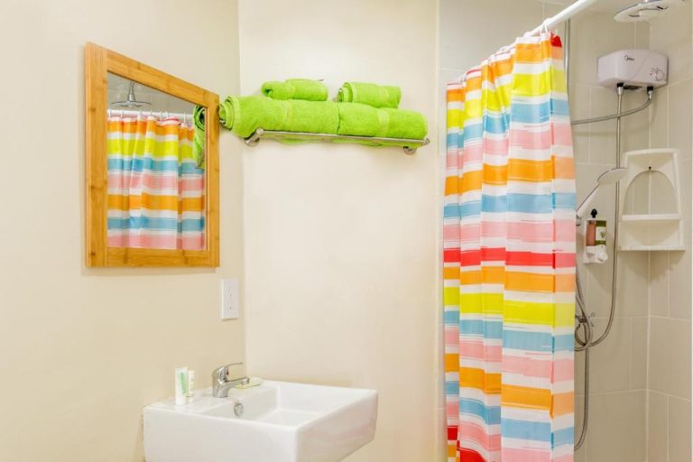 Baño moderno con cortina de ducha multicolor y toallas verdes en Serene by the Sea