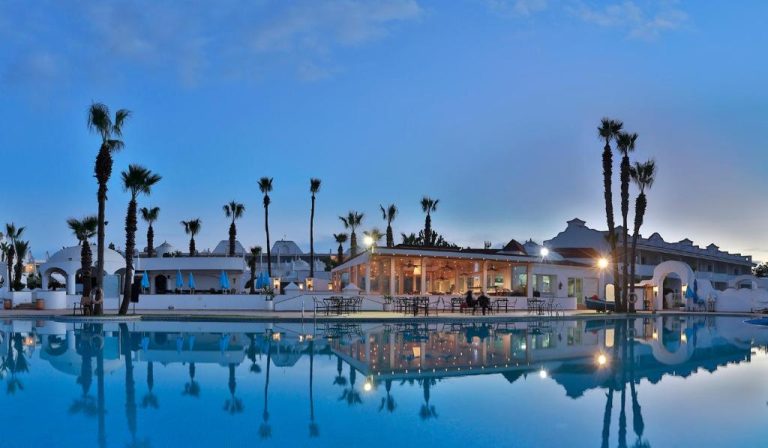Piscina exterior iluminada al atardecer del L'Amphitrite Palace Beach Resort & Spa con palmeras