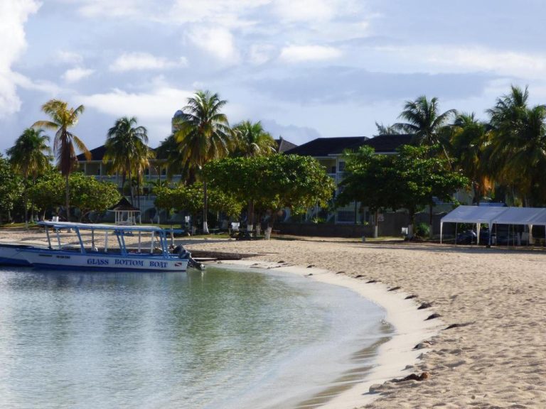 Playa tropical con bote de fondo de cristal frente al Beach One Bedroom Suite A22 con palmeras y hotel