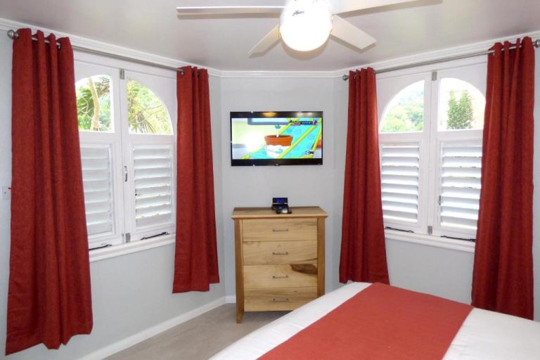 Habitación con televisión, cómoda de madera y cortinas rojas en Beach One Bedroom Suite A22