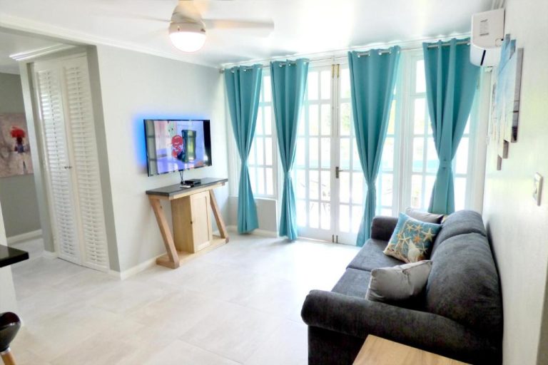Salón luminoso con sofá, televisor y cortinas turquesas en Beach One Bedroom Suite A22