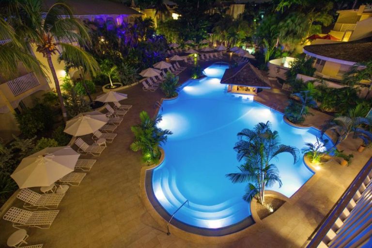 Piscina iluminada de noche con tumbonas y palmeras en Sugar Bay Barbados All Inclusive