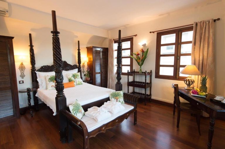 Habitación colonial con cama de dosel de madera tallada y suelo de parqué en Hotel l'Impératrice