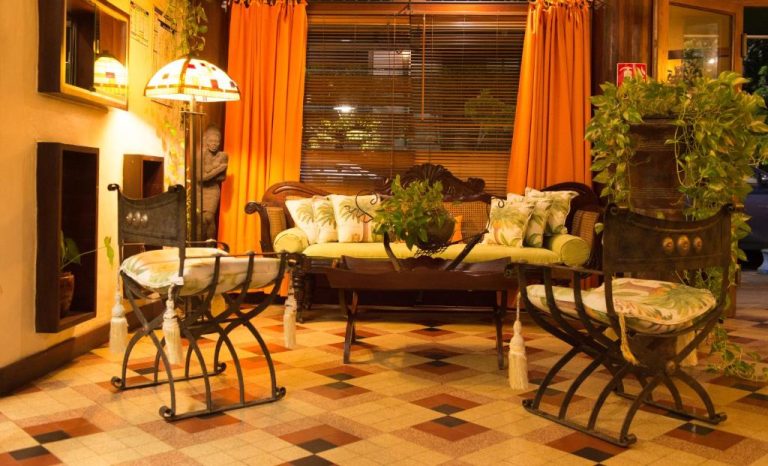 Elegante salón colonial con sofá de madera tallada y sillas de hierro forjado en Hotel l'Impératrice